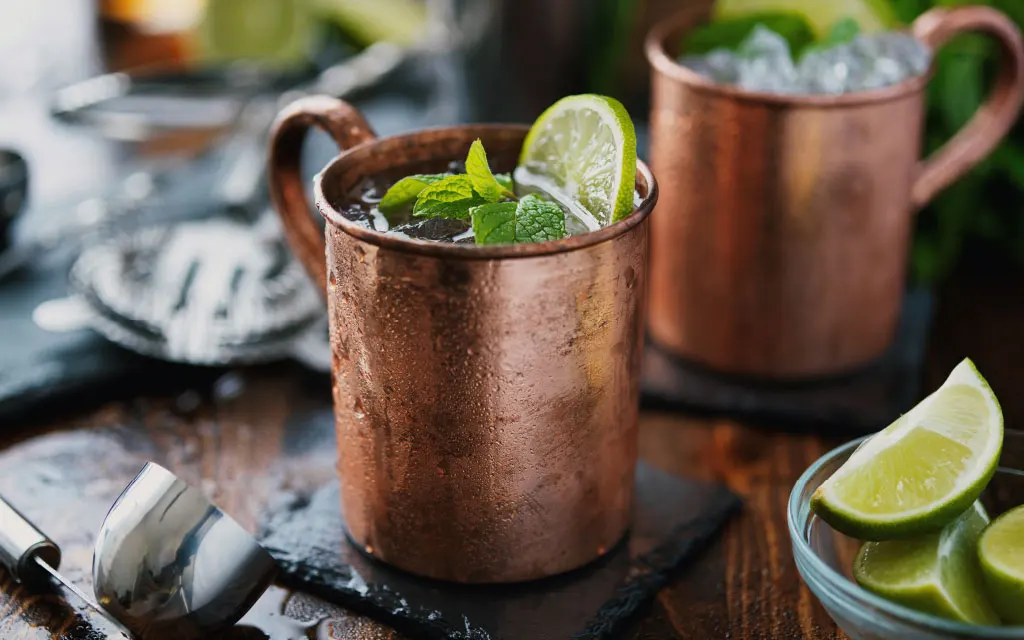 Copper cup with vodka cocktail inside and ingredients around it. 