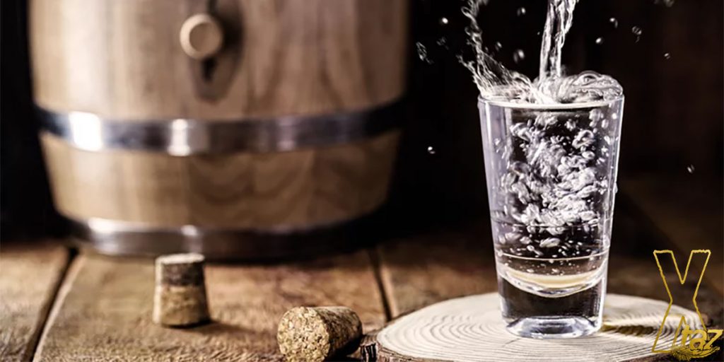 A glass with vodka on a wooden table and a barrel on background.